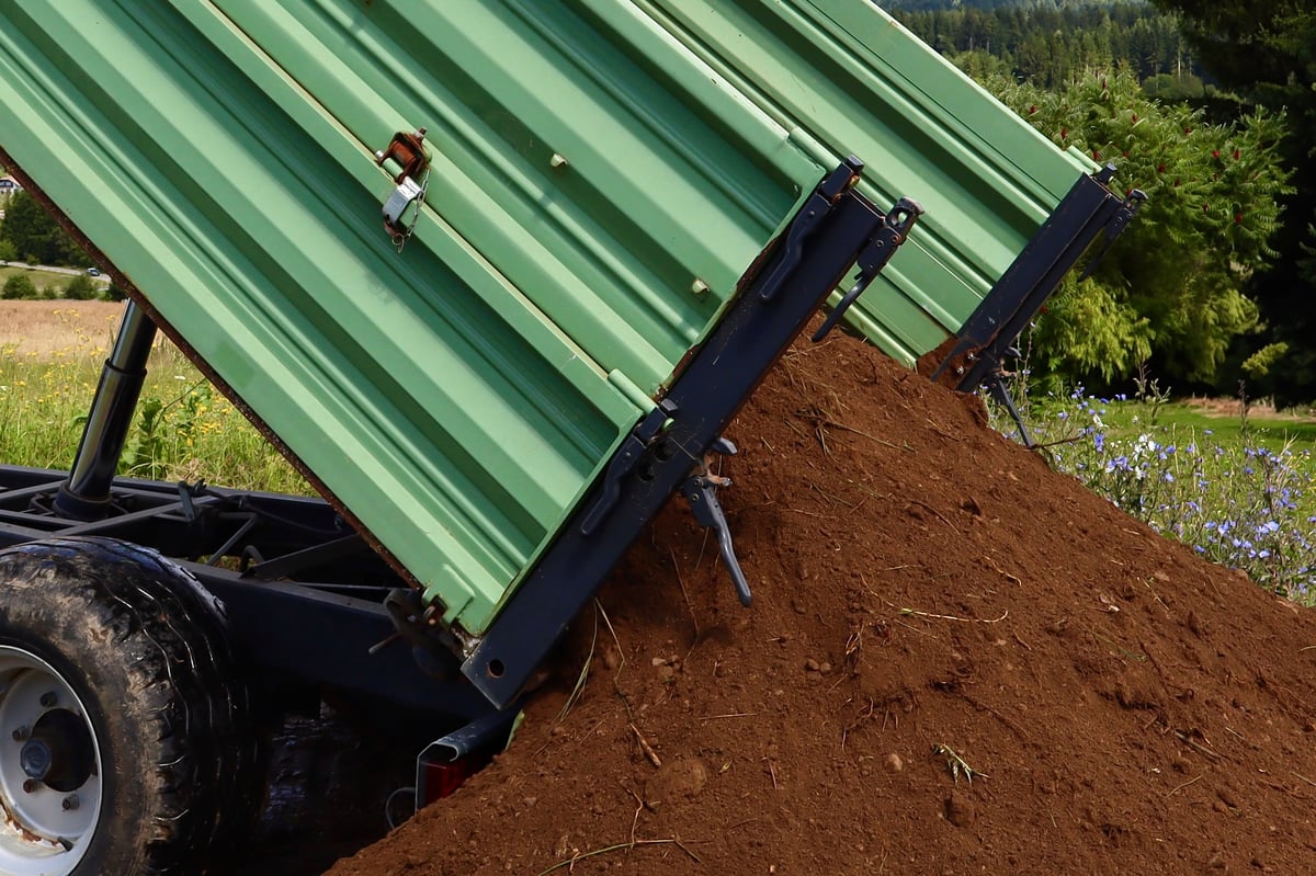 Green trailer unloading a pile of soil onto the ground on a farm field