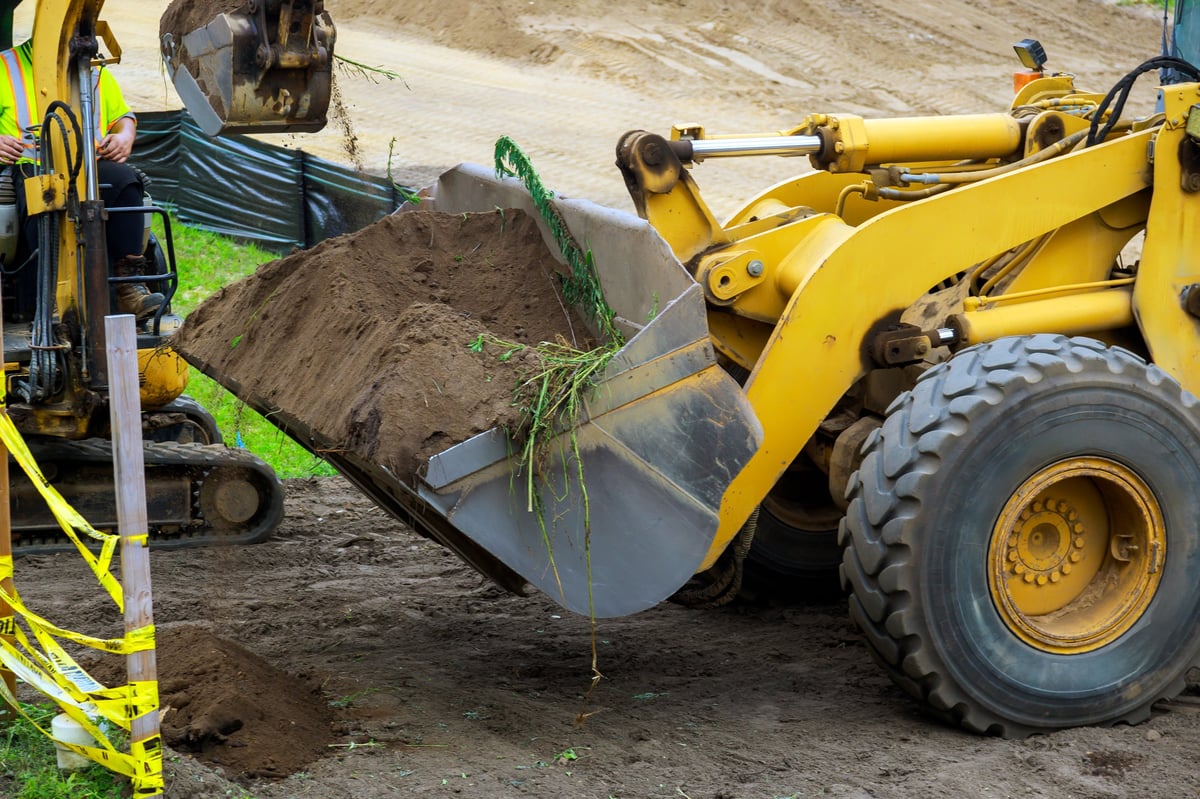 Workers operate construction machines to dig soil move dirt at building site