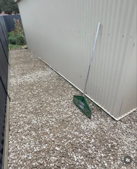 Narrow gravel pathway between white corrugated metal walls with a green object on the ground