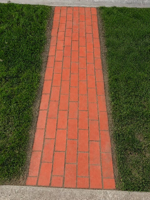 Red brick walkway running between green grass with concrete edges