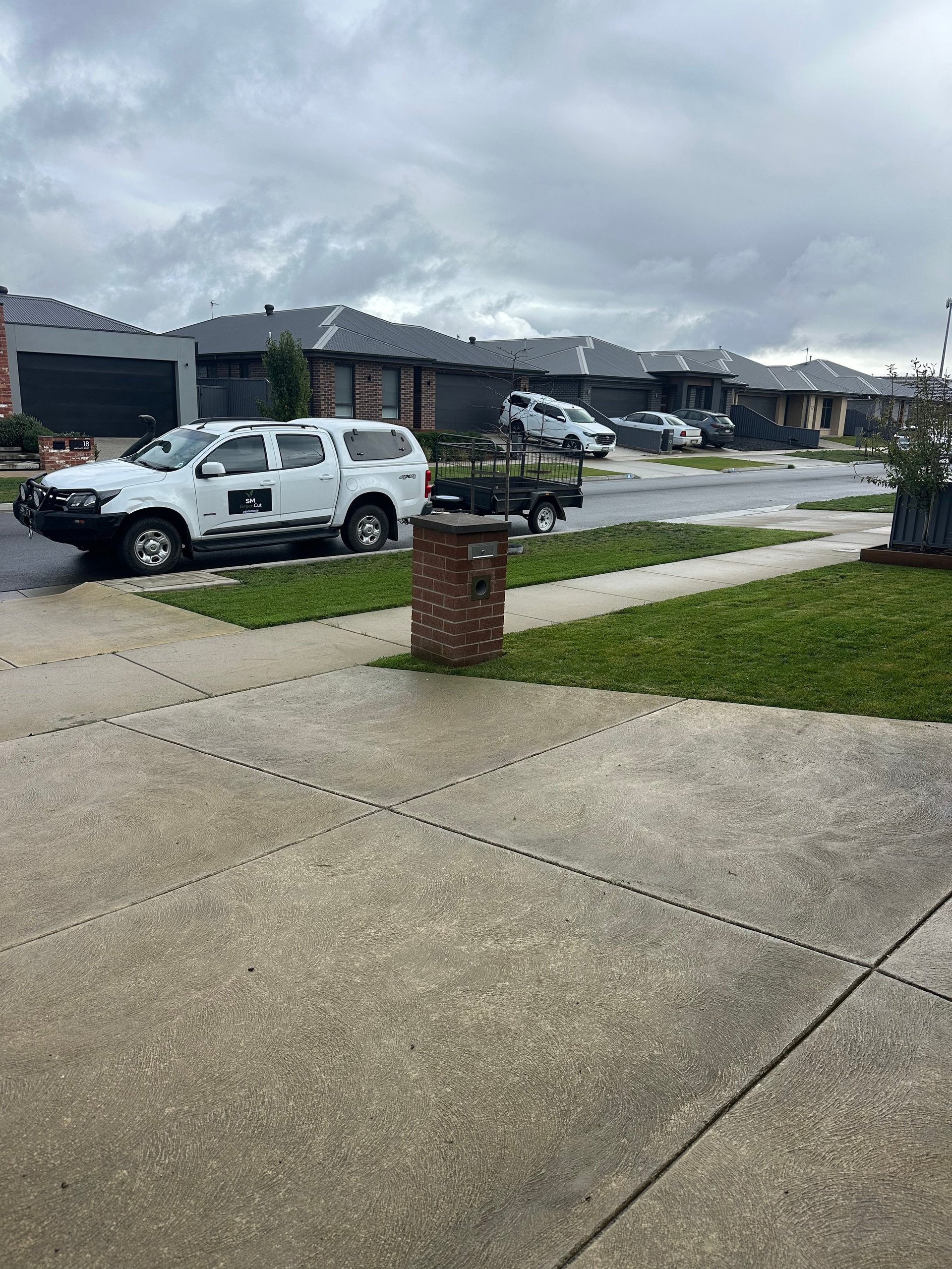 White utility ute parked in suburban driveway with brick mailbox, modern homes and cloudy sky in background