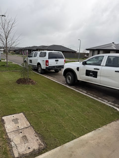 Two white utility vehicles parked on a residential street with green lawn and modern homes in background