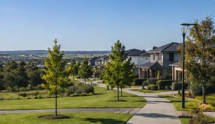 Large two-story stone house with manicured lawn, young trees, and driveway in a sprawling residential development with valley views