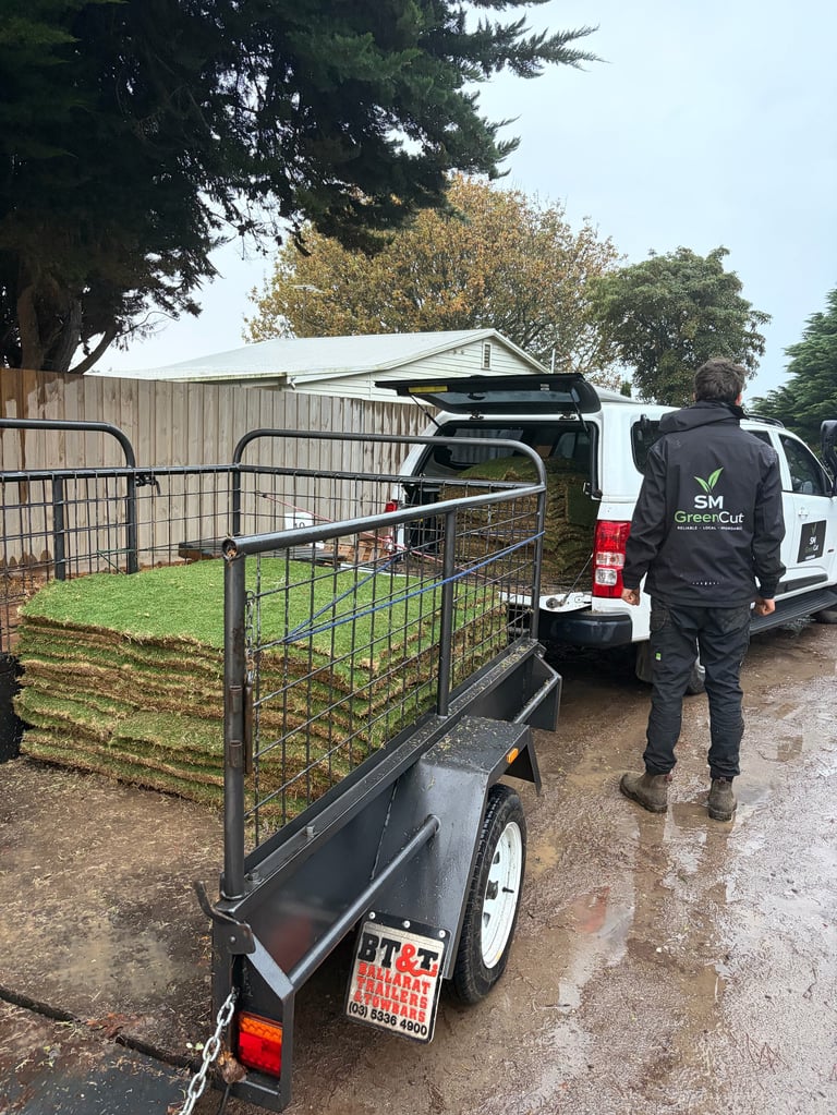 Metal livestock trailer with gate attached to white van on wet gravel driveway next to wooden fencing and trees